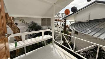 Ein Balkon mit weißer Reling, einer Holztür und Blick auf den Himmel sowie die umliegenden Gebäude.