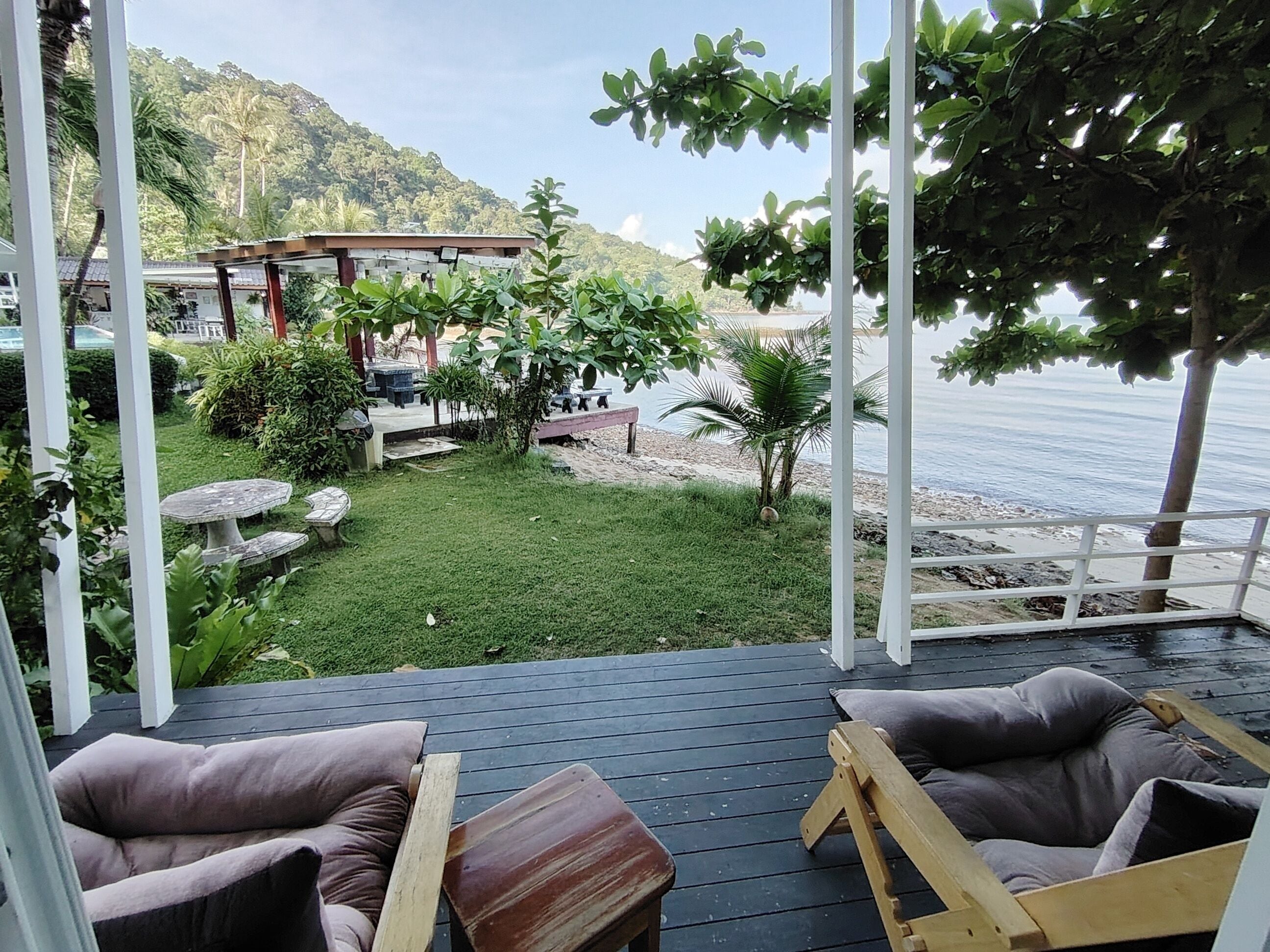 Una terraza con sillas y una mesa de madera, con vistas a un área verde con una piscina pequeña y un edificio al fondo.