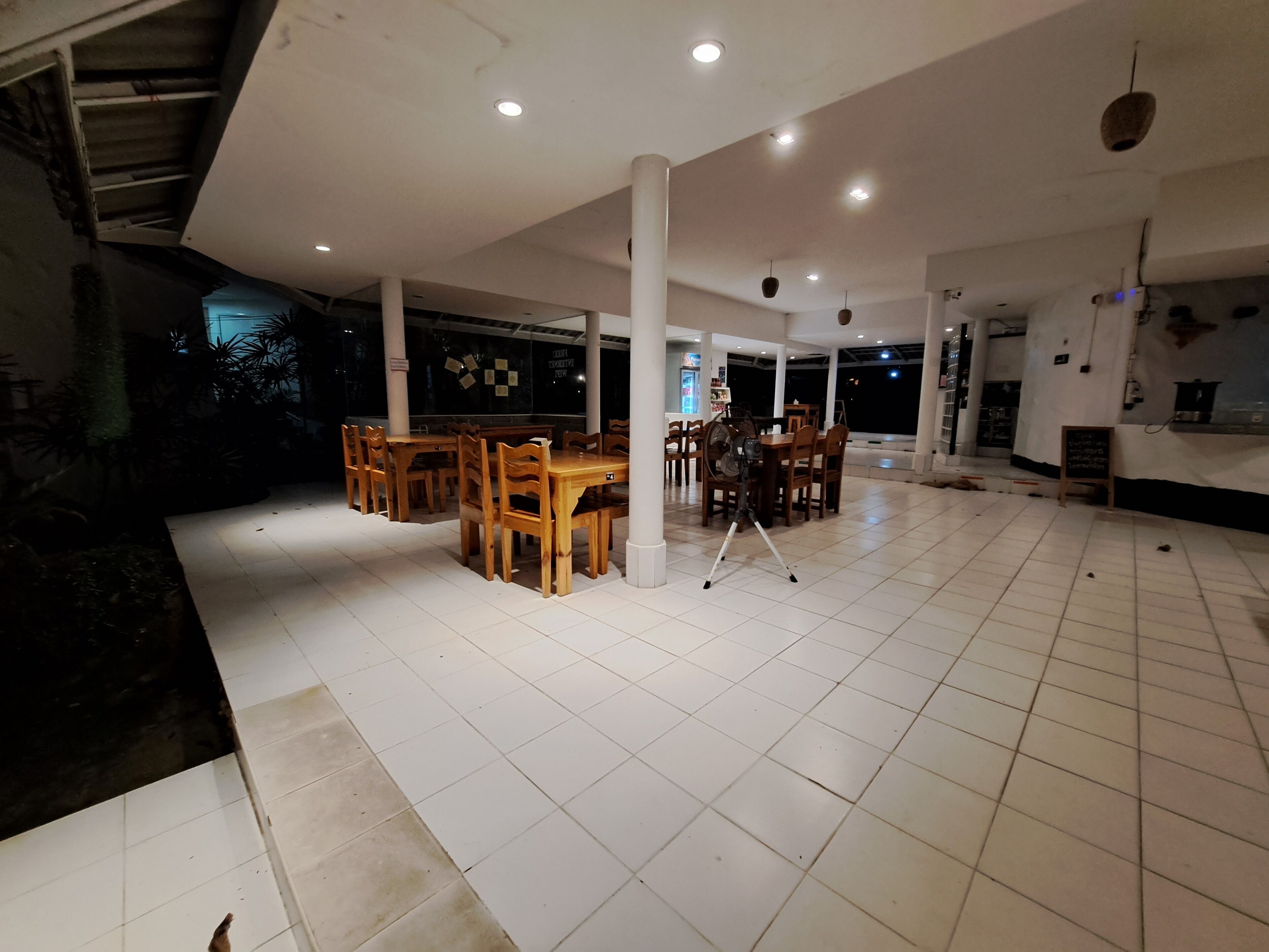 Un'ampia area interna con pavimento piastrellato, tavoli e sedie in legno e diverse luci a soffitto.