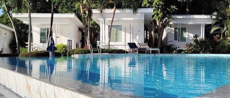 A swimming pool with lounge chairs, surrounded by palm trees and white buildings.