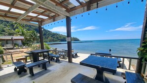 An outdoor seating area with tables and benches, overlooking a body of water and a distant island. - White house bailan resort (Ko Chang)