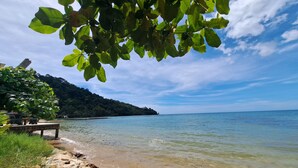 A beach with clear water, a rocky shoreline, and a forested hill in the background. - White house bailan resort (Ko Chang)