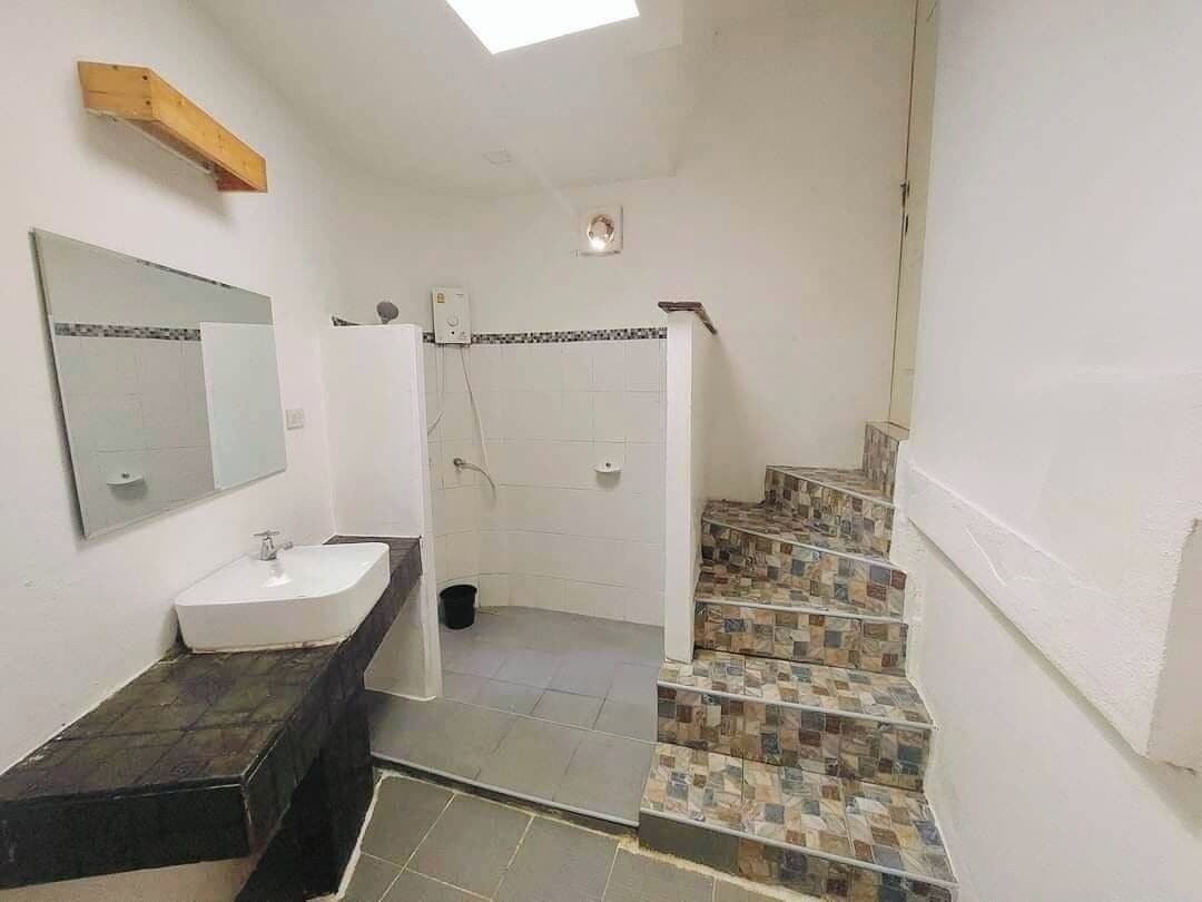 A bathroom with a white sink, a mirror, and a shower. There is a staircase with patterned tiles leading to another room.