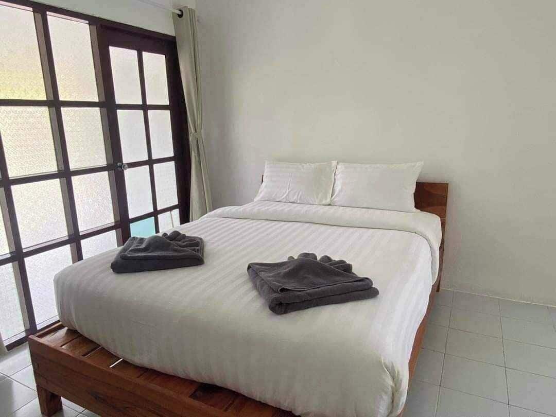 A neatly made bed with white linens and two folded dark towels on a wooden bed frame.