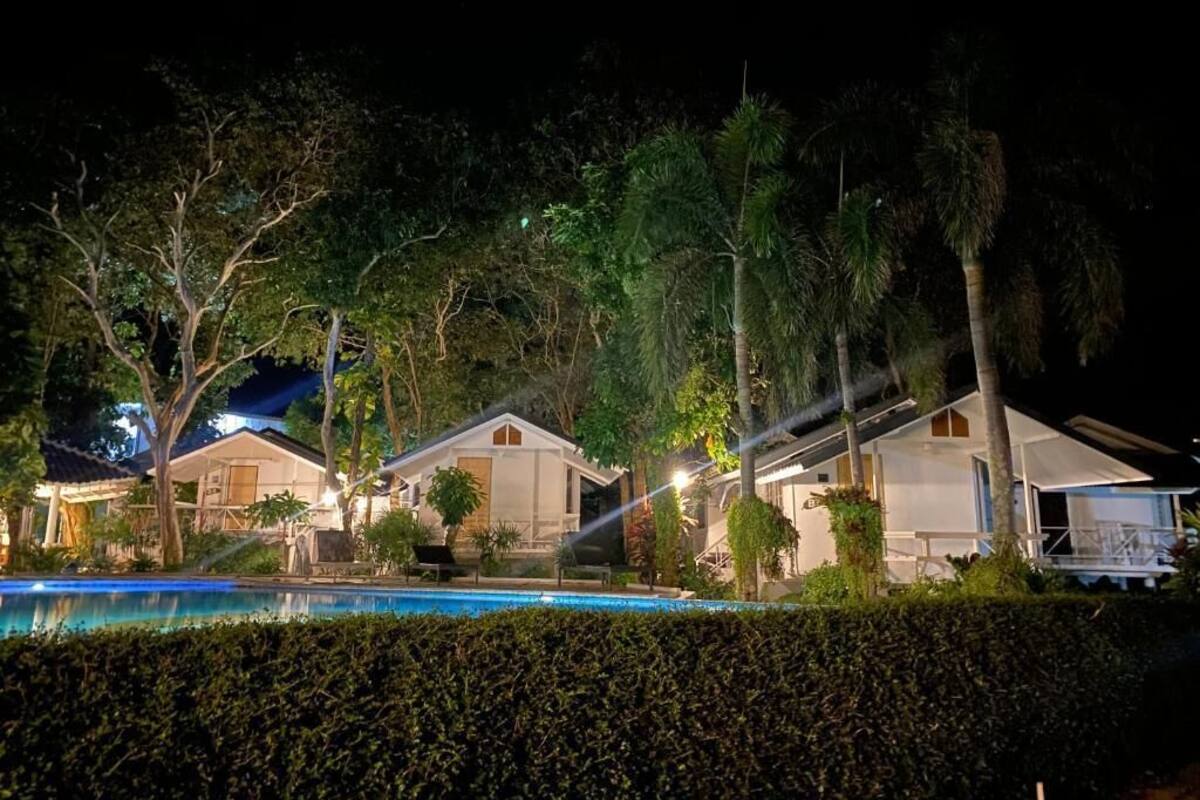 A nighttime view of a resort with multiple bungalow-style accommodations, a swimming pool, and lush greenery.