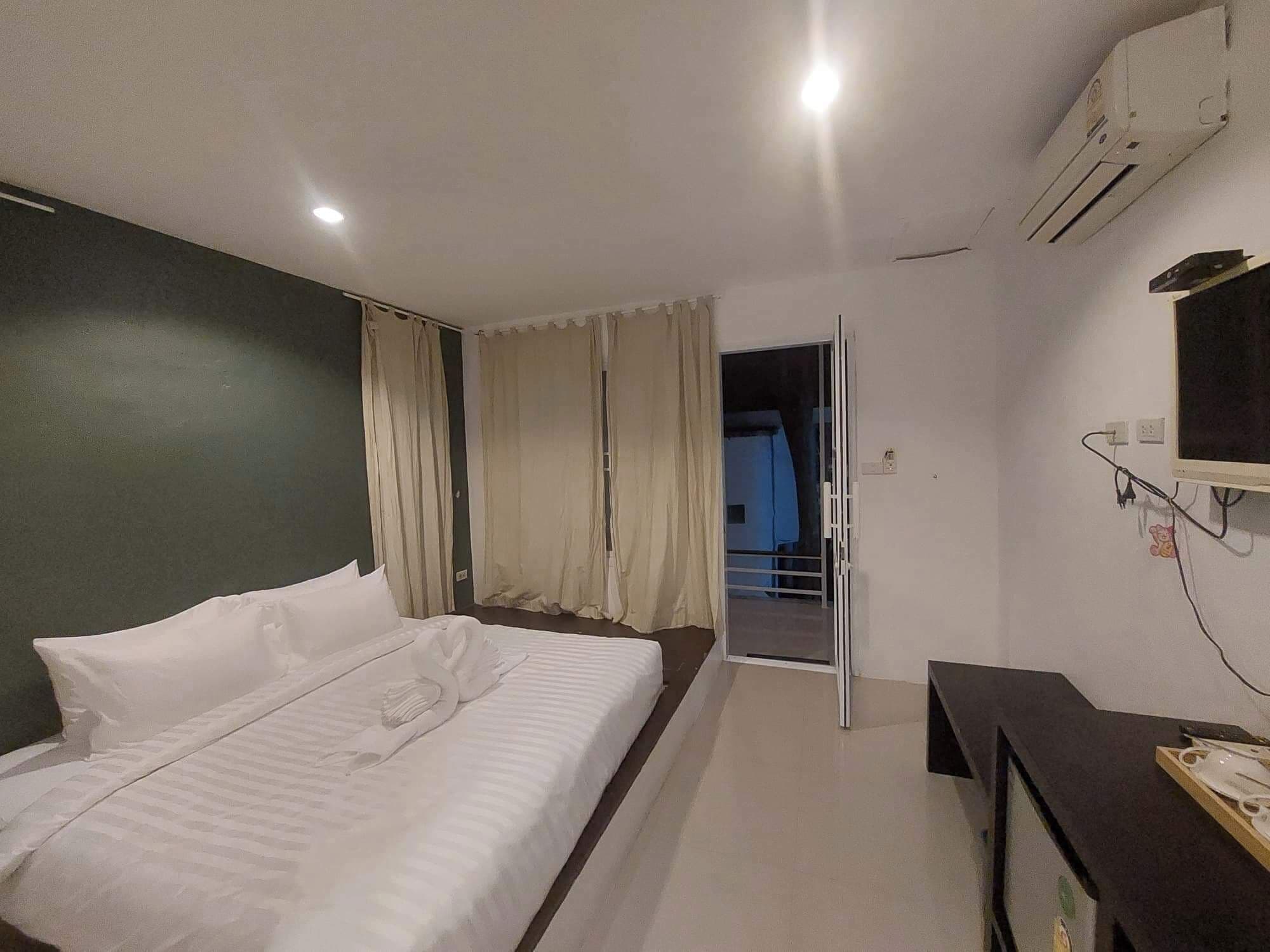 A hotel room with a bed, a desk, an air conditioner, and a view of the outside.