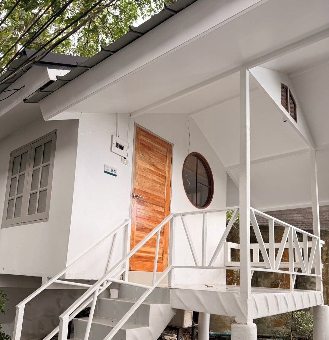 A white building with a wooden door, a window, and a balcony with white railings.
