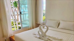 A hotel room with a bed, a window with curtains, and a view of palm trees. - White house bailan resort (Ko Chang)