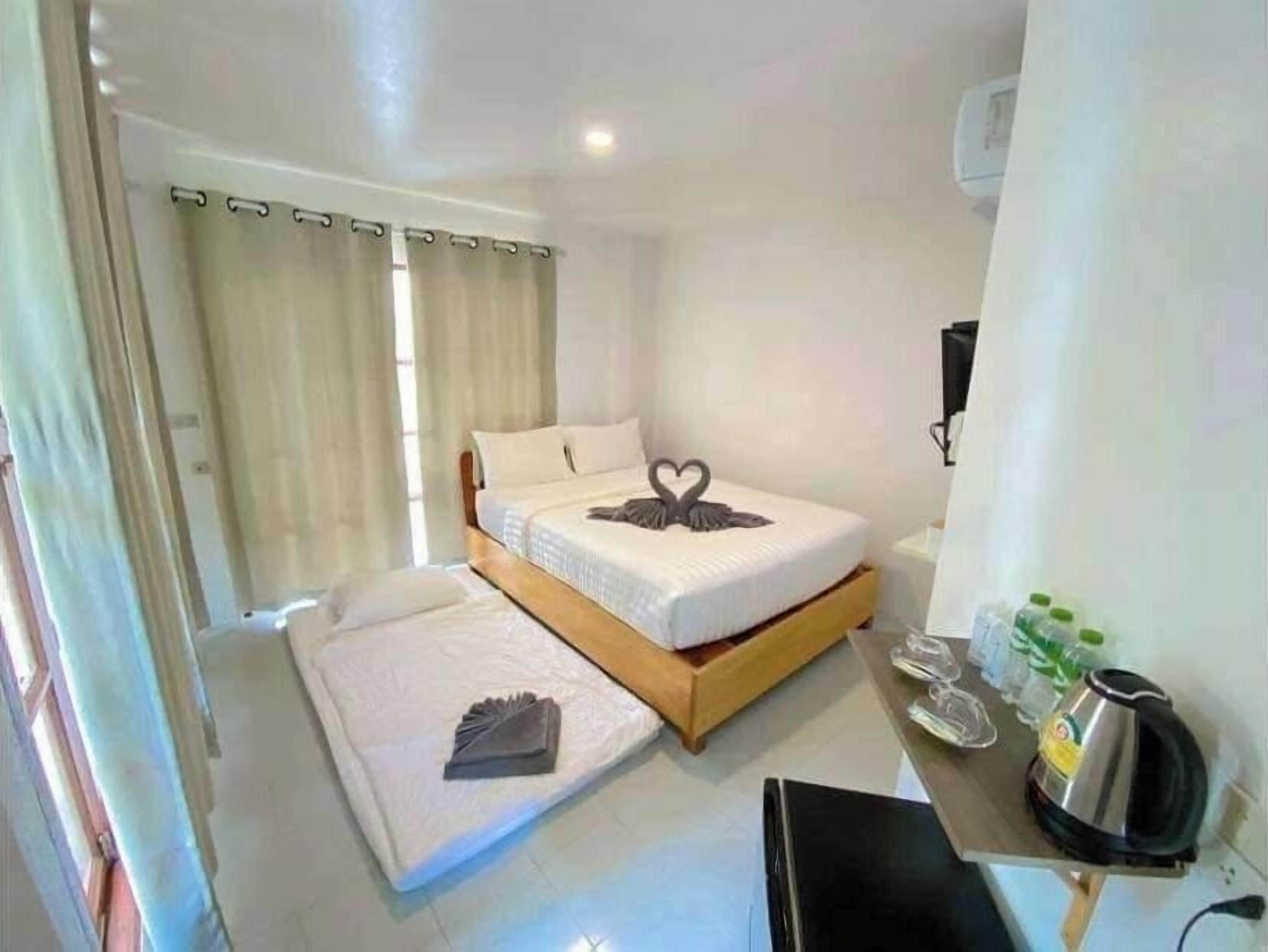A hotel room with a bed, a bedside table with a kettle, and a TV.