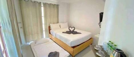 A hotel room with a bed, a bedside table with a kettle, and a TV.