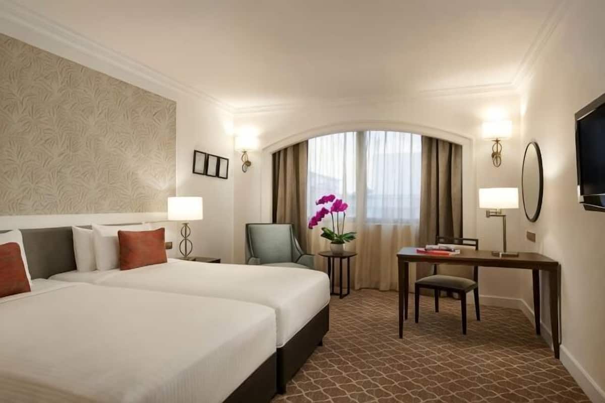 A hotel room with two beds, a desk, a chair, a TV, and a window with curtains.