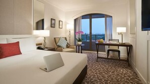 A hotel room with a bed, a desk, a chair, a laptop, a balcony with a view, and a TV.