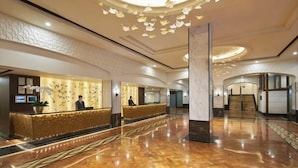 A spacious lobby with a marble floor, a reception desk, and a modern chandelier.