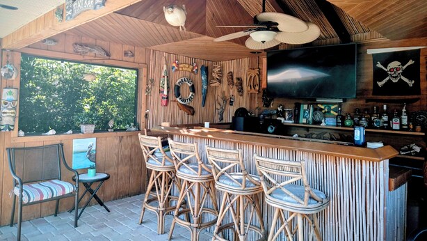 A tiki bar with wooden walls, a bar counter, and several wicker chairs. -   Great 4-bedroom house in Englewood with pool, on a canal, 15 min. from beach. (Englewood)