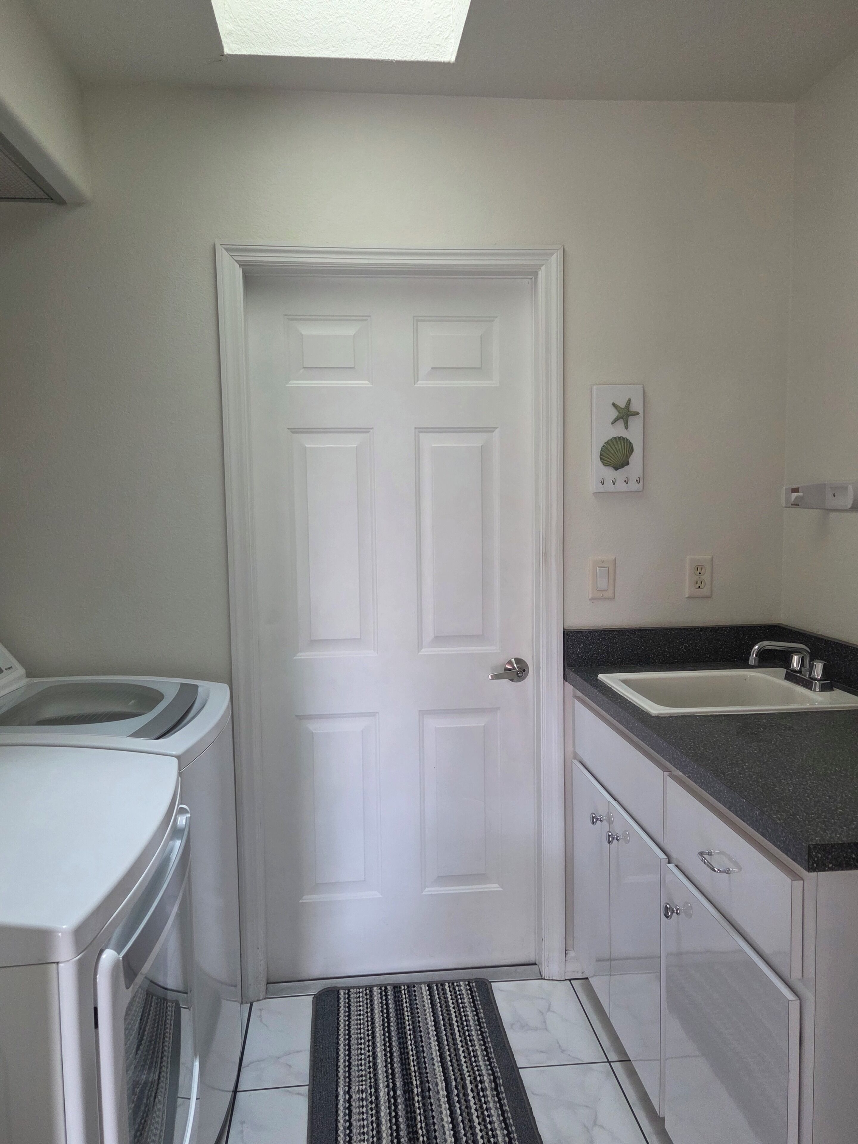 Uma cozinha compacta com porta branca, máquina de lavar embutida, pia e chão revestido de azulejos.