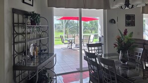 A dining area with a glass table, chairs, a red umbrella, and a view of the outdoors. -   Great 4-bedroom house in Englewood with pool, on a canal, 15 min. from beach. (Englewood)