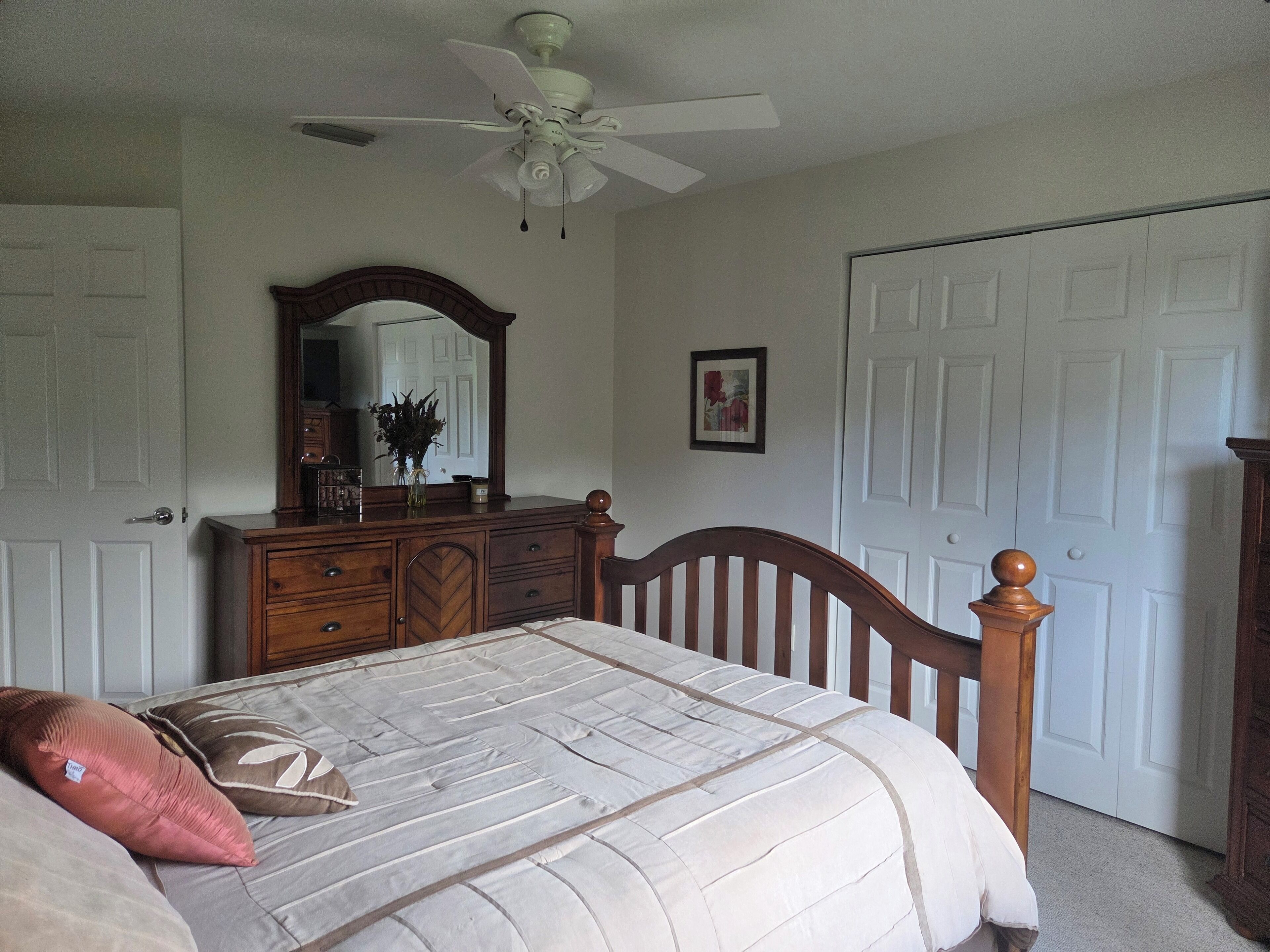 A bedroom with a bed, dresser, mirror, ceiling fan, and white doors.