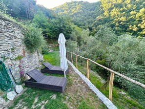 A stone wall, two wicker lounge chairs, a white umbrella, and a garden with trees and grass. - Manuela by Interhome (Zoagli)
