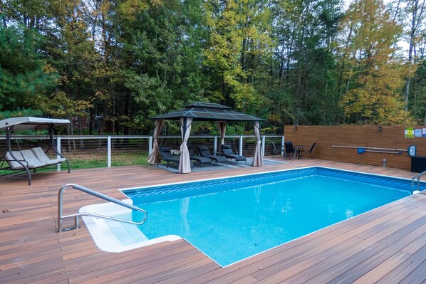 Une terrasse en bois avec une piscine, des chaises longues et un kiosque.