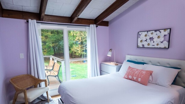 Een slaapkamer met een bed, nachtkastje, stoel, raam met gordijnen en uitzicht op de omgeving.