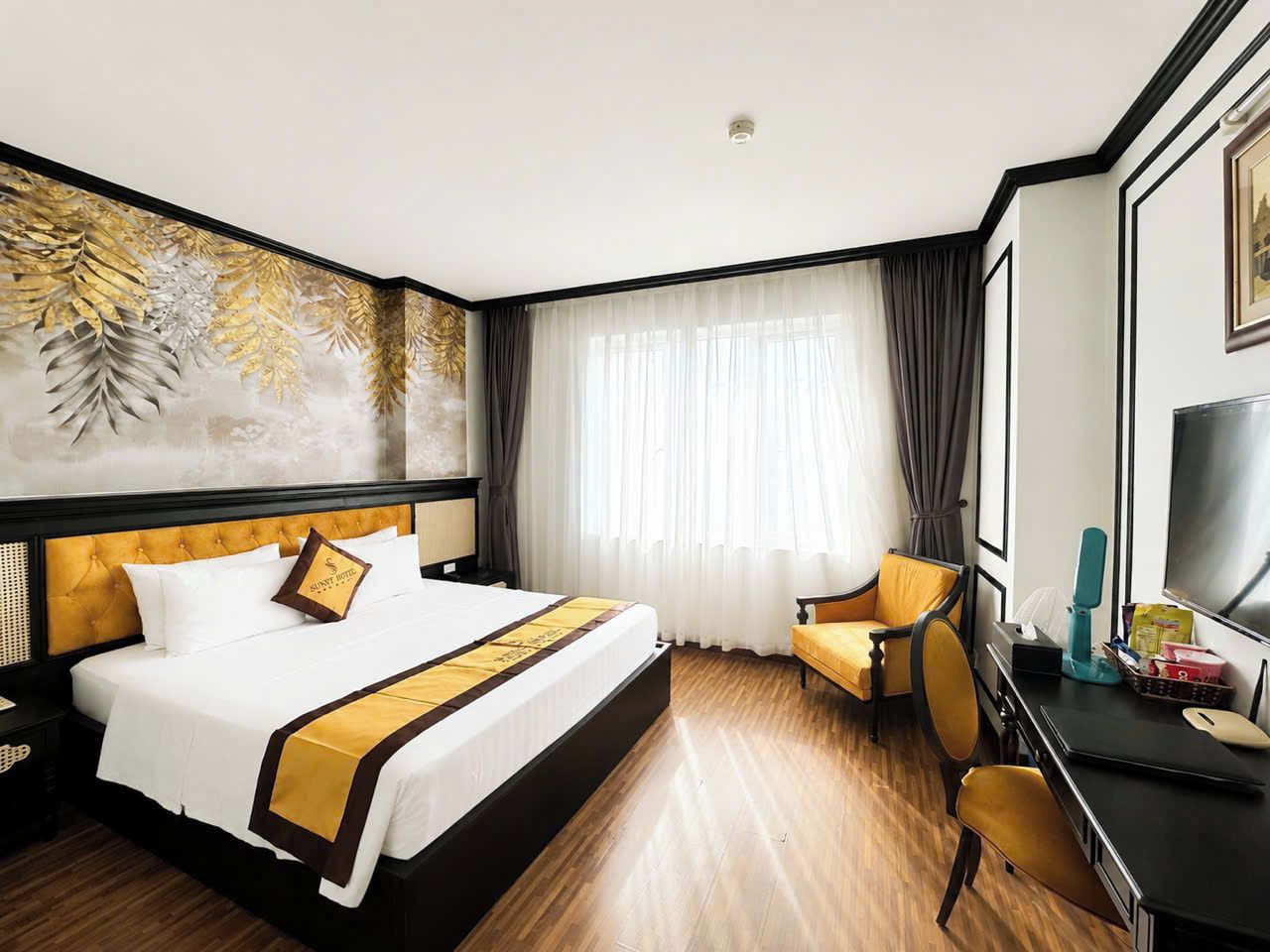 A hotel room with a bed, a desk, a chair, a TV, and a large window with curtains.
