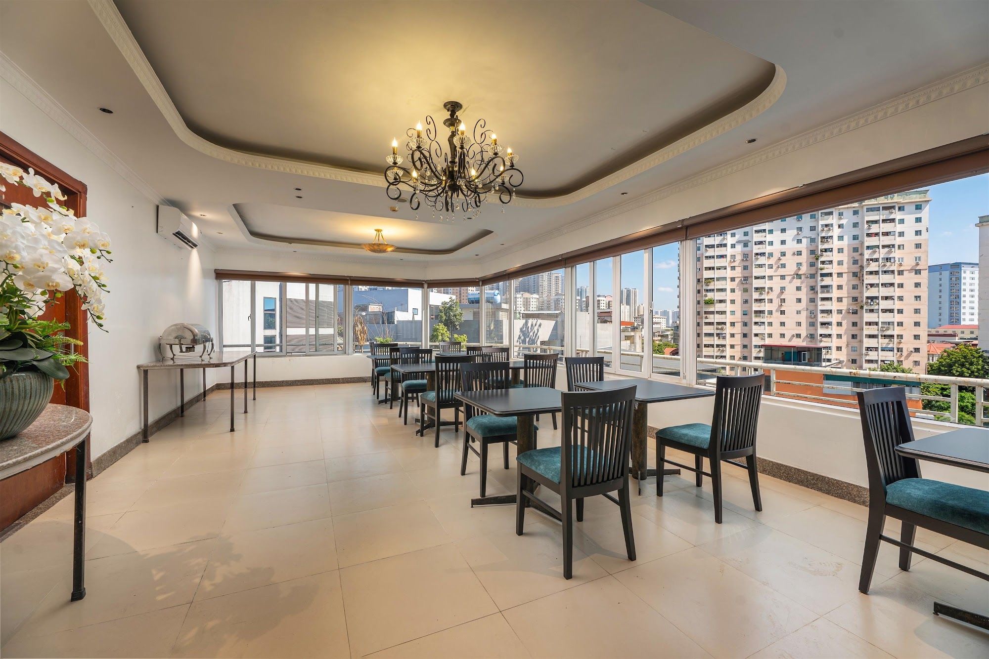 A spacious dining area with tables and chairs, a chandelier, and large windows offering a city view.