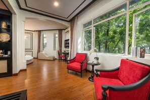 A hotel room with a wooden floor, a red sofa, a small table with a book, and a large window with a view of trees. - Sunny Hotel Ha Noi (Hanoi)
