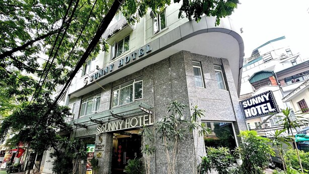 Un hotel con un llamativo letrero que dice 'Sunny Hotel', una fachada curva y plantas en macetas a lo largo de la entrada.