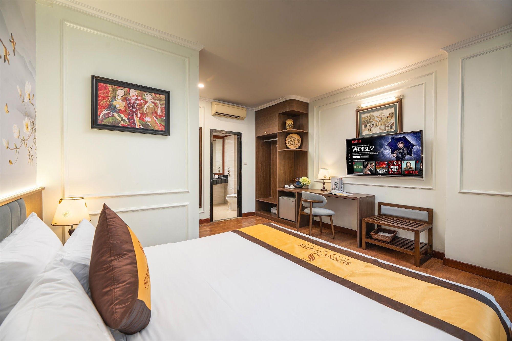 Ein Hotelzimmer mit Bett, Schreibtisch, Fernseher und einem durchgehenden Tür sichtbaren Badezimmer.