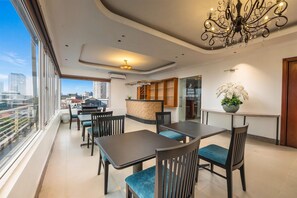 Una habitación de hotel con balcón, un comedor con mesas y sillas, un candelabro y una recepción.