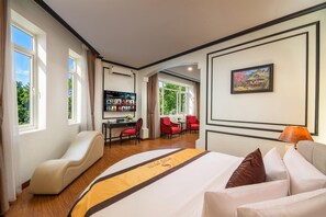 Habitación de hotel con cama, escritorio, dos sillas, televisor y un cuadro en la pared.