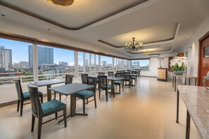 Un comedor amplio con mesas y sillas, ventanas grandes con vistas a la ciudad y un candelabro.