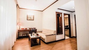 Una habitación de hotel con suelo de madera, un sofá, un escritorio con lámpara y un cuadro en la pared.