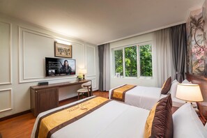 A hotel room with two beds, a desk with a television, a window with a view of greenery, and a painting on the wall. - Sunny Hotel Ha Noi (Hanoi)