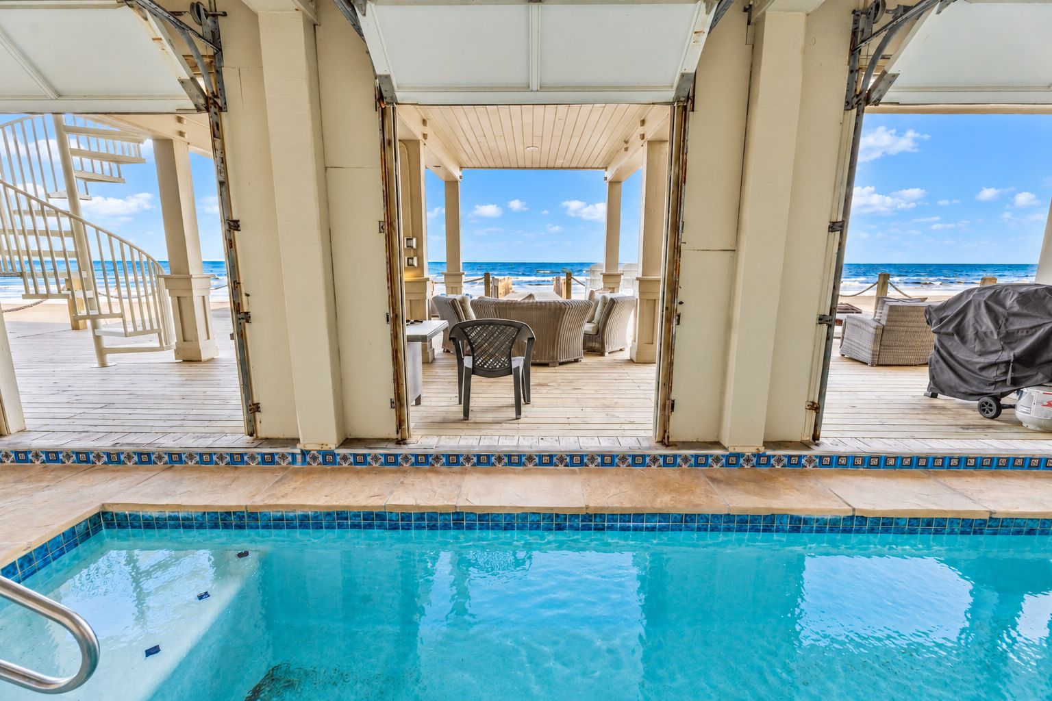 A pool area with a view of the ocean, outdoor seating, and a covered deck.