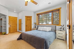A bedroom with a bed, a window, a ceiling fan, and wooden doors.