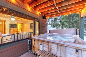 A wooden cabin with a hot tub, wooden deck, and a view of the snowy landscape.