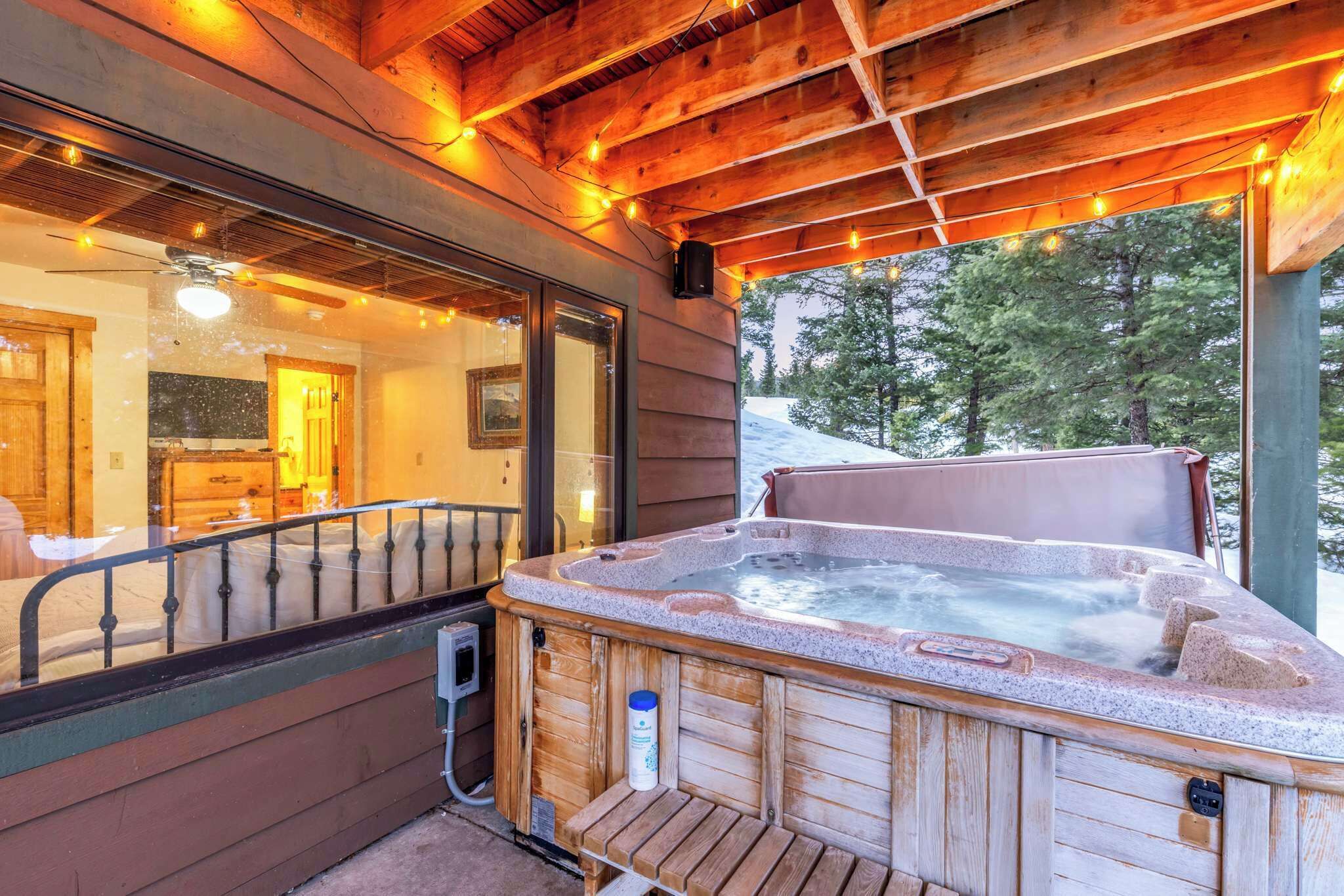Een houten hut met een hottub, houten terras en uitzicht op het besneeuwde landschap.
