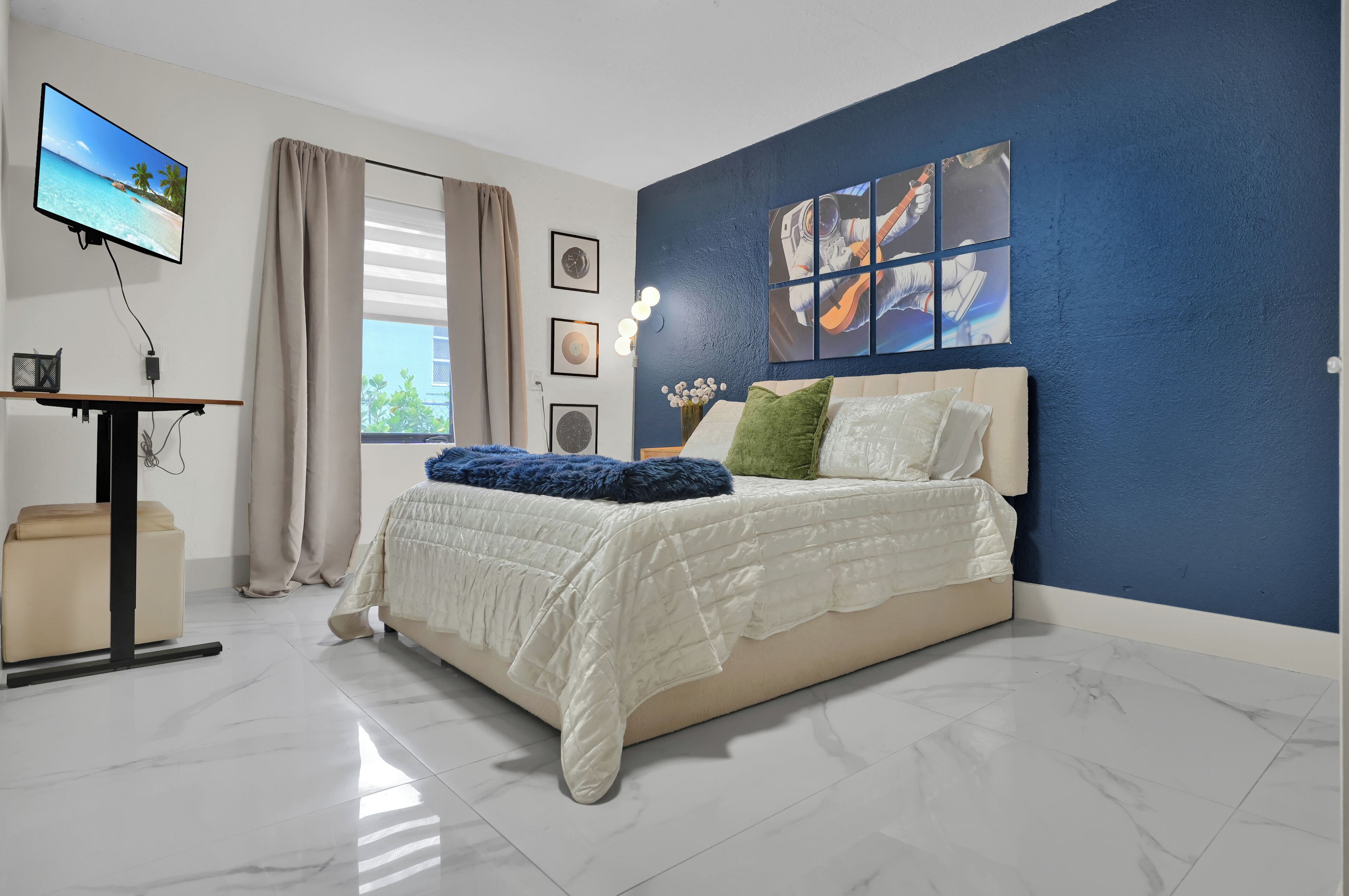 A bedroom with a bed, a TV, a desk, and a window with curtains.