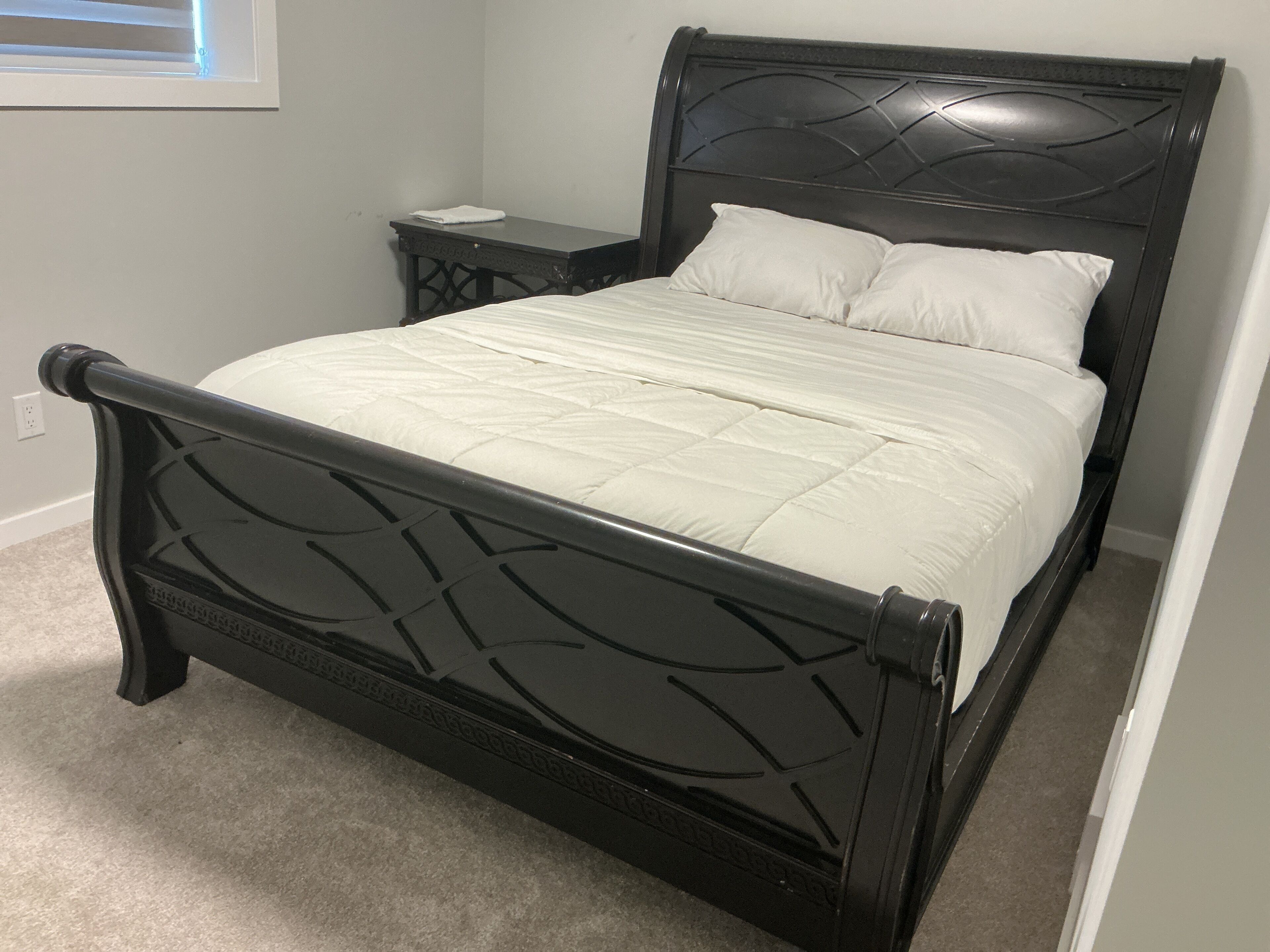 A black metal bed frame with a quilted white mattress and two pillows.