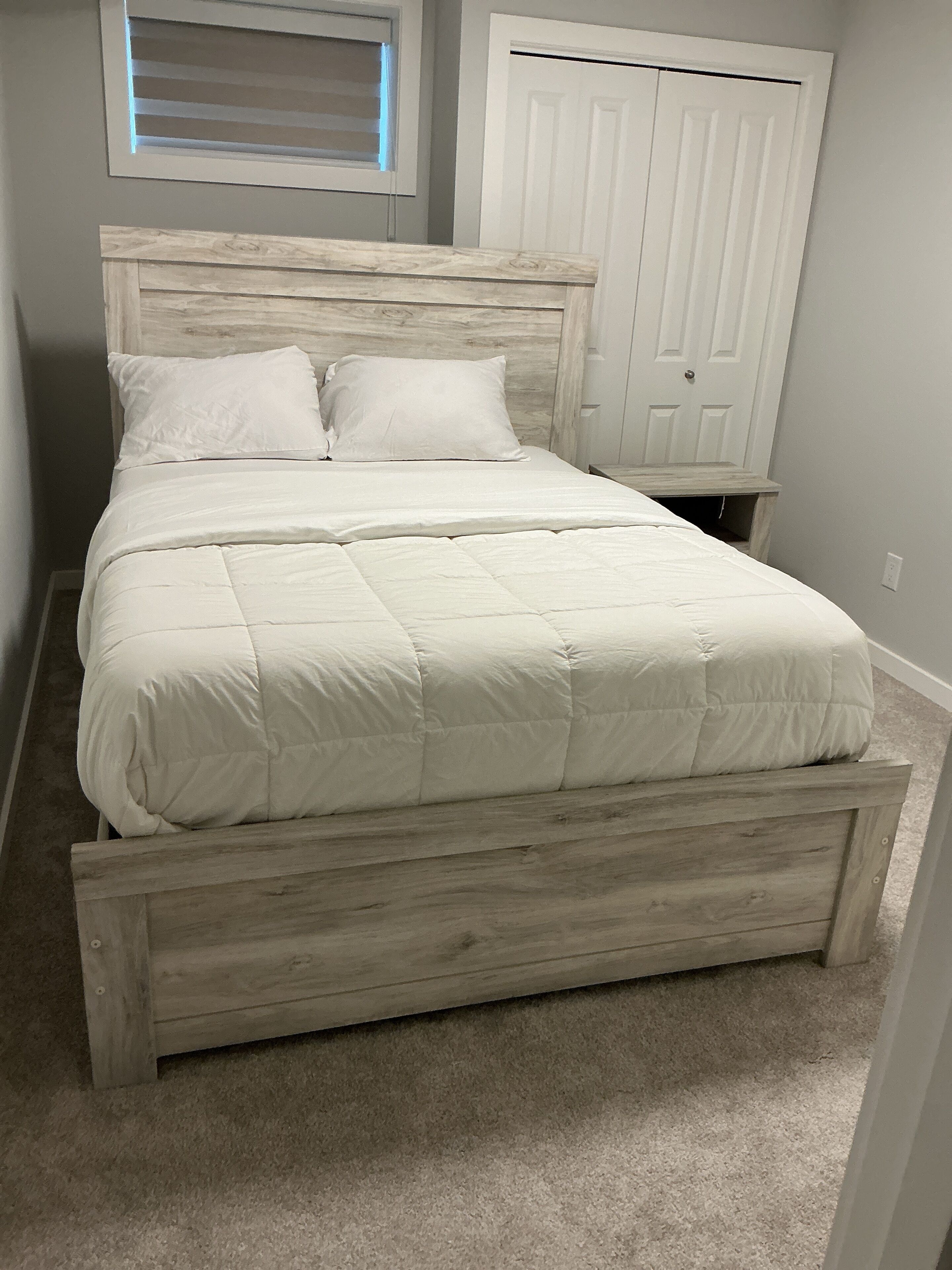 A bed with a wooden headboard and footboard, a white comforter, and two pillows.