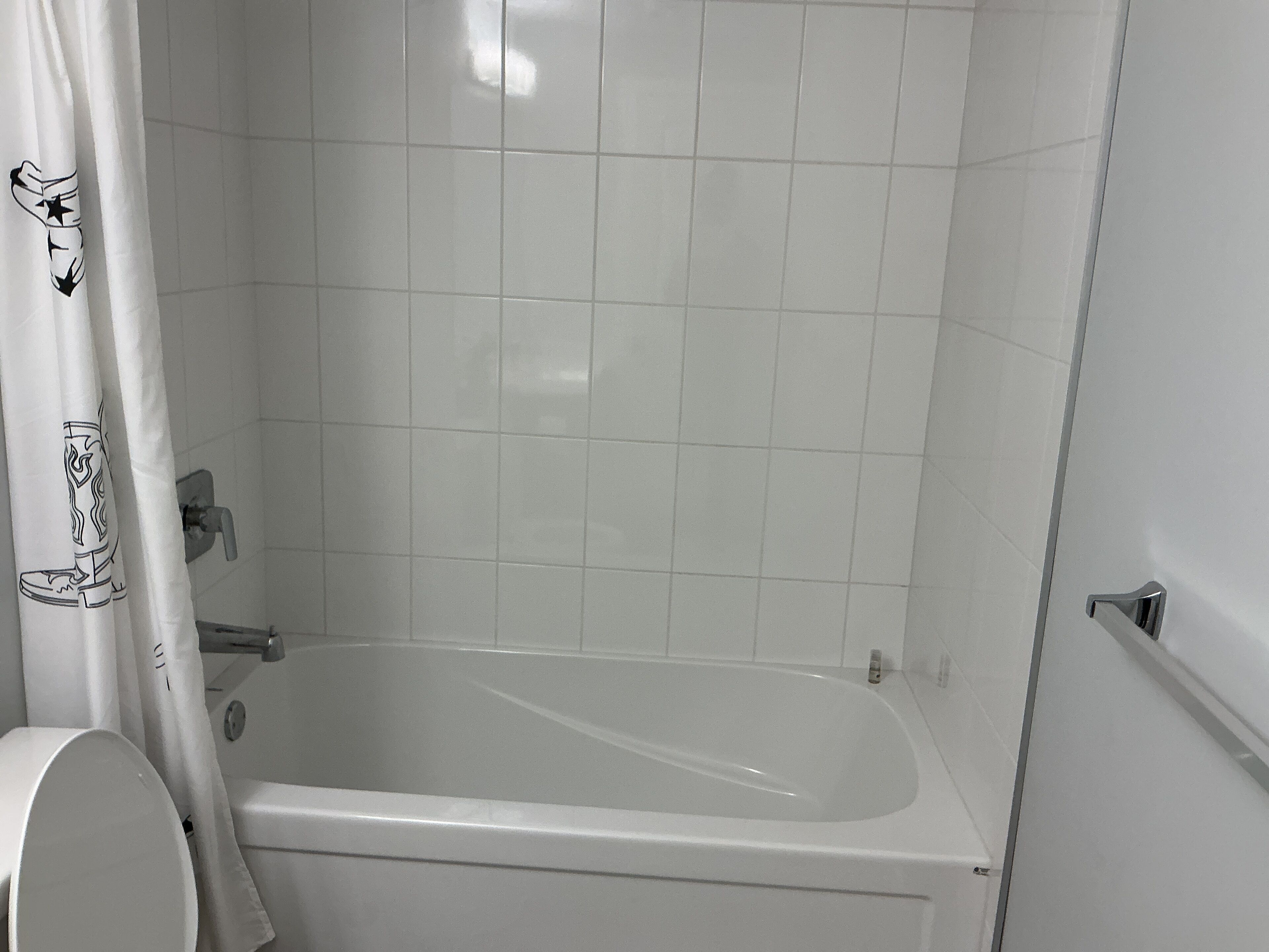 Une salle de bain avec une baignoire, des carreaux blancs et un rideau de douche orné d’un motif de cowboy.