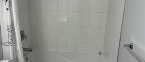 A bathroom with a bathtub, white tiles, and a shower curtain with a cowboy design.