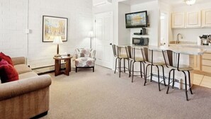 A living room with a sofa, a coffee table, a lamp, and a chair. There is a dining area with a table and chairs. A TV is mounted on the wall above the dining area. - Welcoming studio with access to Sundance Film Festival, ski resorts in Park City (Park City)
