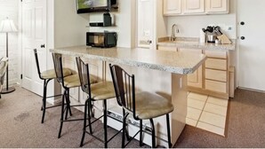A kitchen with a granite countertop, three bar stools, a microwave, a television, and wooden cabinets. - Welcoming studio with access to Sundance Film Festival, ski resorts in Park City (Park City)