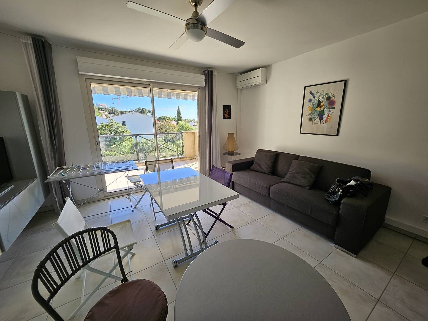 A living room with a sofa, a glass dining table, a TV, and a ceiling fan.