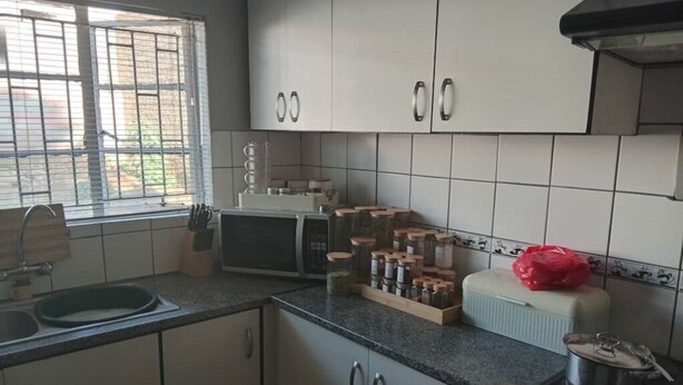 A kitchen with white cabinets, a microwave, a sink, and a window with blinds. - Welcoming Bed & Breakfast with Air Conditioning in the Heart of Windhoek (Windhoek)