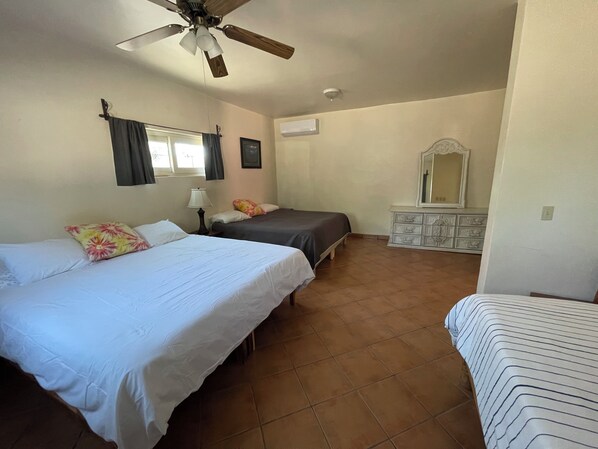 Una habitación con dos camas, ventilador de techo, cómoda y ventana con cortinas.