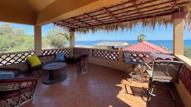 Un espacio de estar al aire libre cubierto con vistas al mar, que cuenta con una mesa redonda, sillas y una planta en maceta.