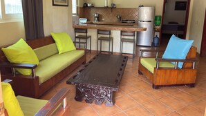 Un espace de vie compact comprenant un canapé, une table basse et un coin repas. On aperçoit également un coin cuisine avec un réfrigérateur, une cuisinière et un évier.